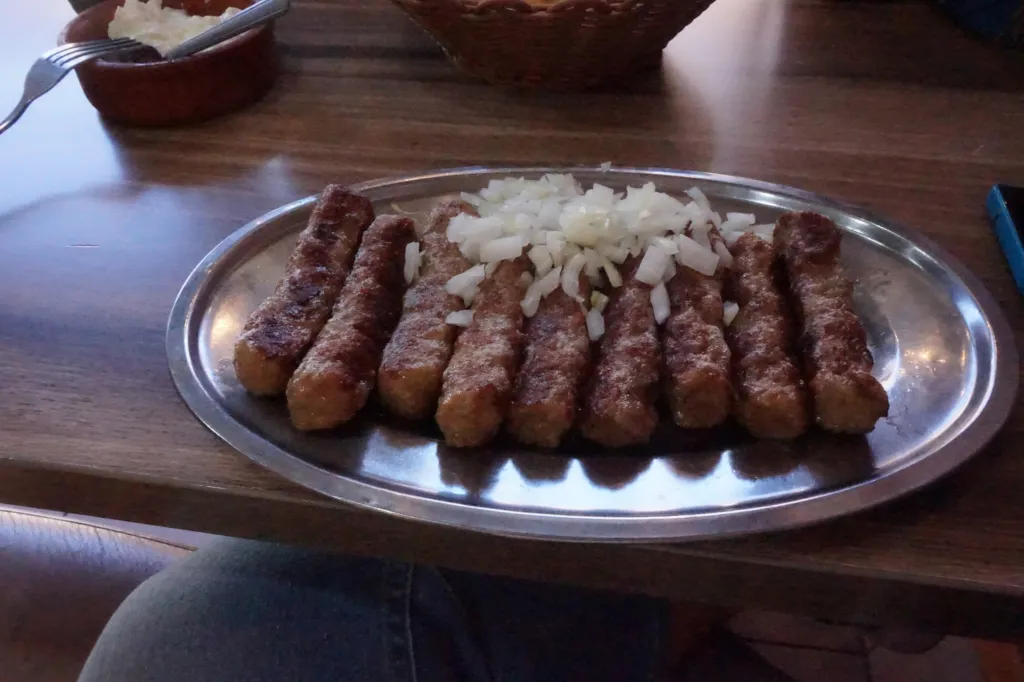 A plate of grilled ćevapi topped with chopped onion