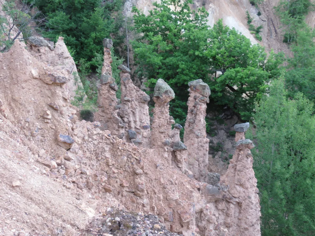 Earth pillars topped with dark stone caps among green trees at Đavolja Varoš