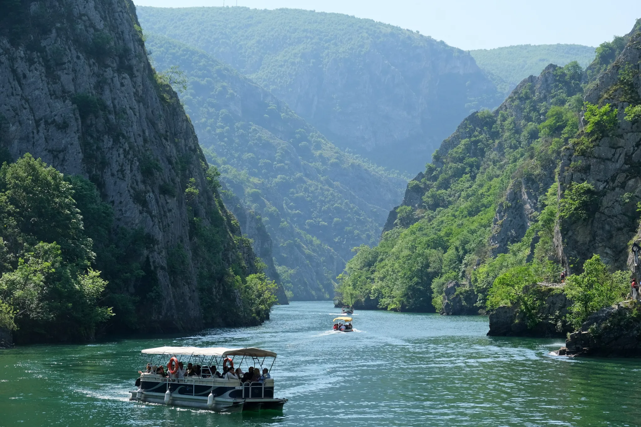 A boat on the green water of the Matka canyon between steep forested cliffs