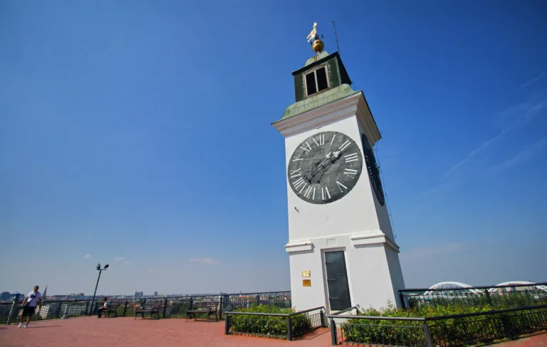 The white clock tower of Petrovaradin Fortress against a blue sky