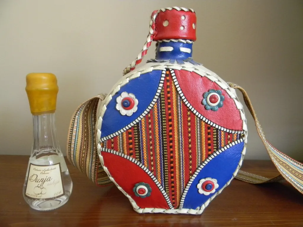 A small bottle of rakija beside a traditional painted wooden flask (čutura)