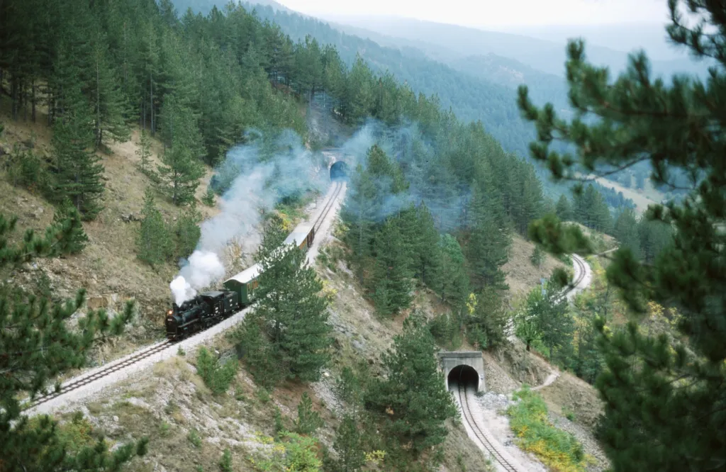 A steam train climbing the loops of the Šargan Eight through forested hills above Mokra Gora