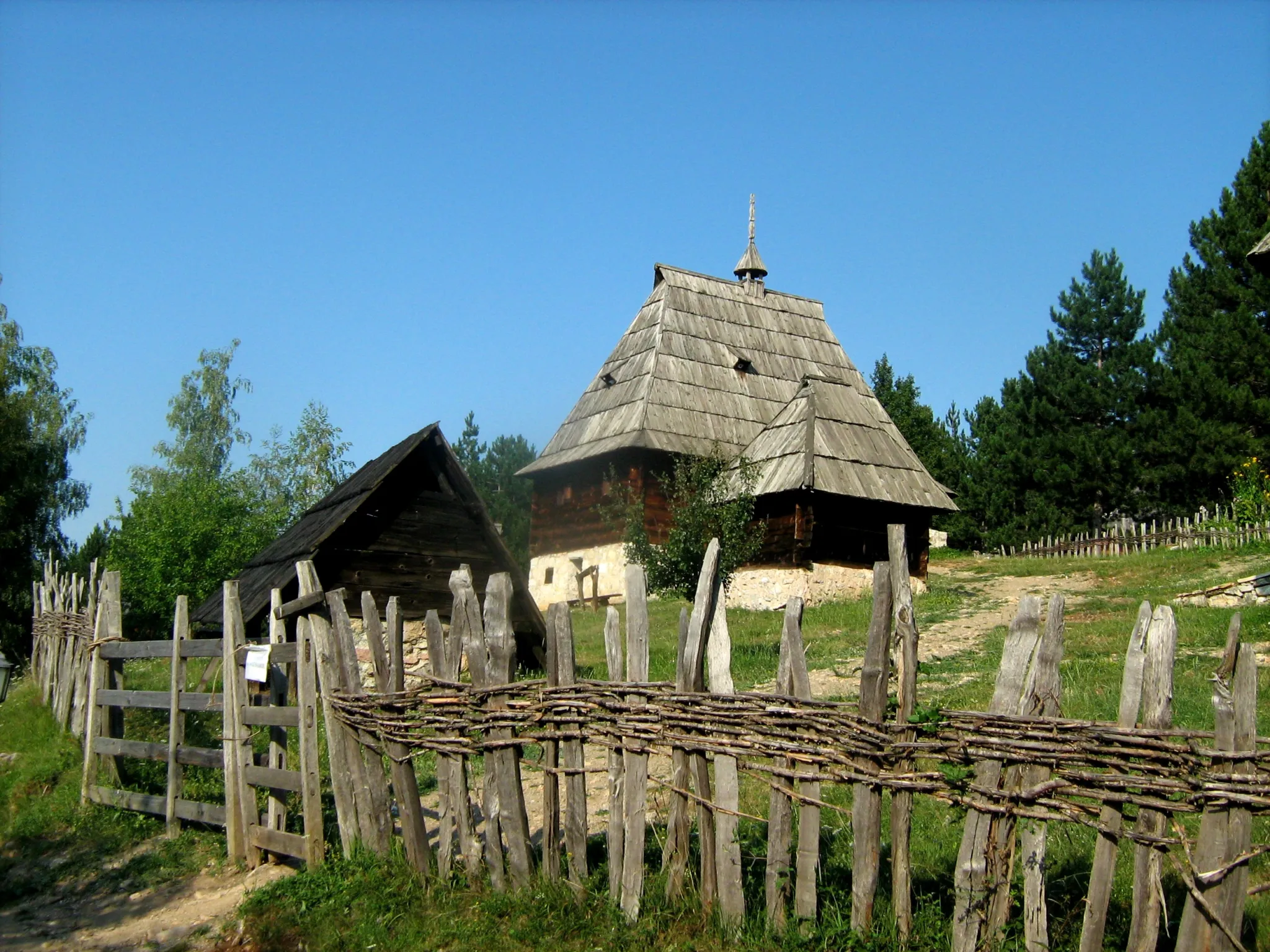 Log houses and a wattle fence on the green hillside of the Sirogojno open-air museum