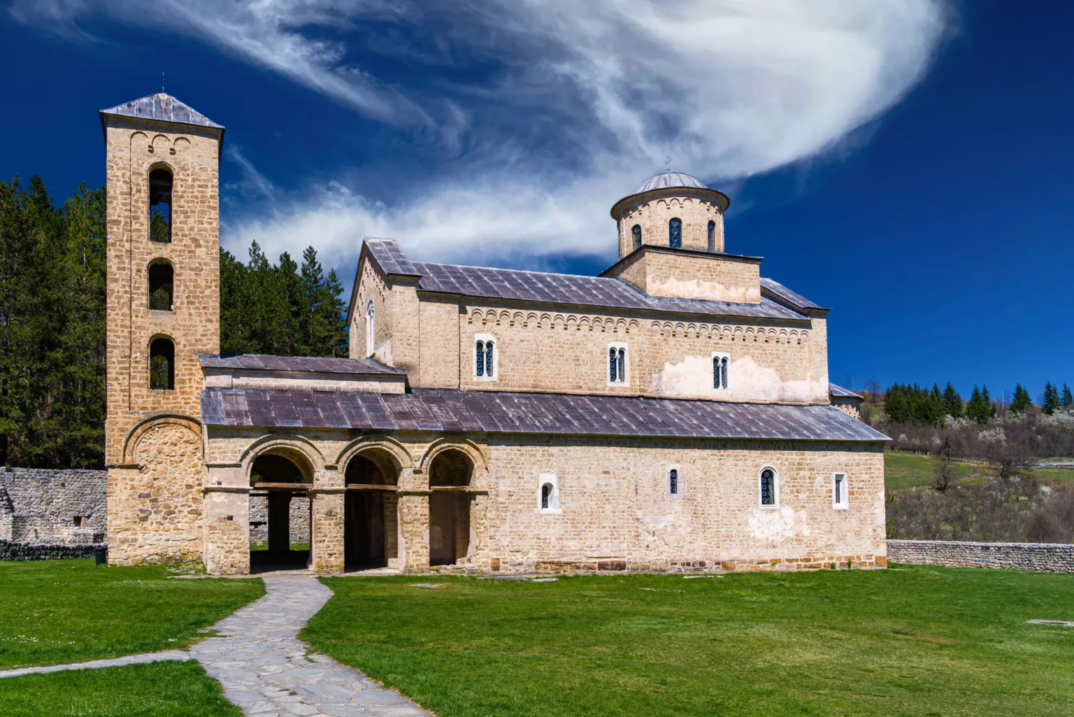 The church and bell tower of Sopoćani Monastery on a green lawn under a blue sky
